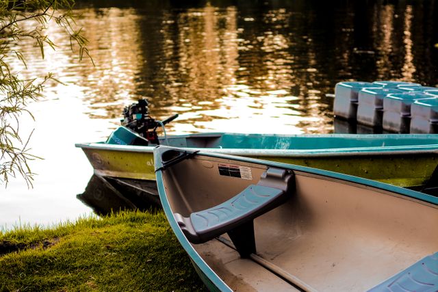 Peaceful scene of empty boat resting near the water's edge of a tranquil lake during sunset. Ideal for use in promotions related to travel, outdoor activities, relaxation, or nature retreats. Also suitable for backgrounds or inspirational content emphasizing calmness and serenity.