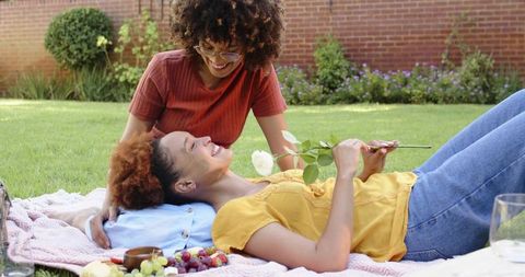African american couple relaxing on picnic blanket in sunny backyard holding white rose