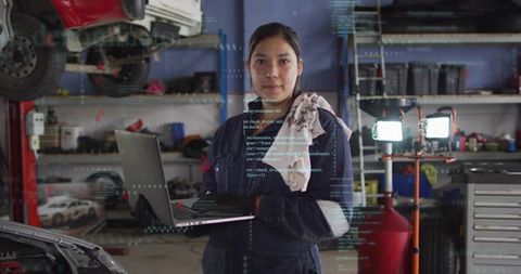 Female automotive technician holding laptop performing digital diagnostics in workshop