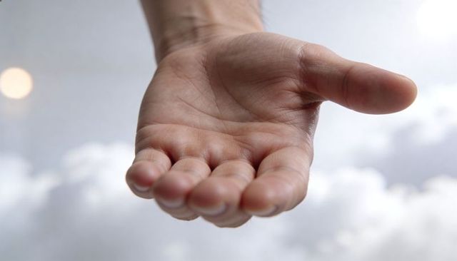 Open right palm reaching forward over soft cloud backdrop with warm bokeh light