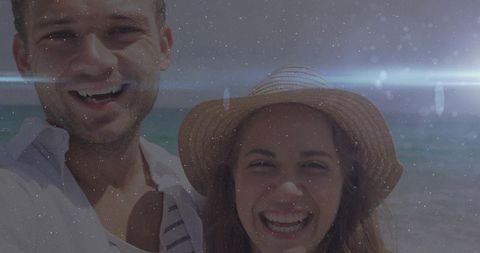 Smiling couple taking selfie on sunny beach with straw hat and lens flare