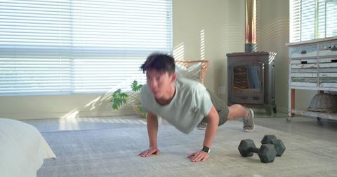 Asian man doing push-ups in sunlit living room wearing smartwatch and workout gear