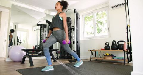 African American woman performing dumbbell lunge in modern home gym for strength training