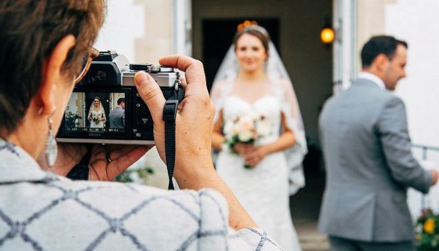 Photographer holding mirrorless camera framing bride in white gown at church entrance