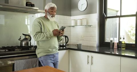 Senior man relaxed in modern kitchen checking smartphone
