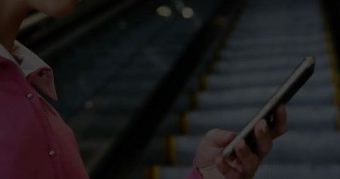 Commuter in pink coat using smartphone on escalator