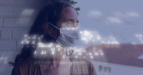 Woman wearing surgical mask looking out window with digital data overlay over rooftops