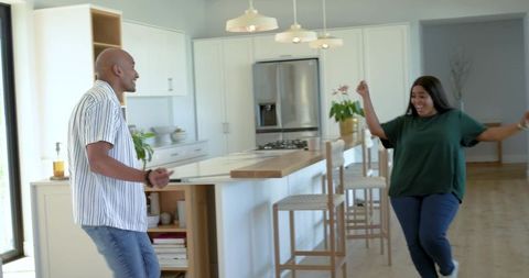 Diverse couple running toward each other in modern kitchen with island and pendant lights
