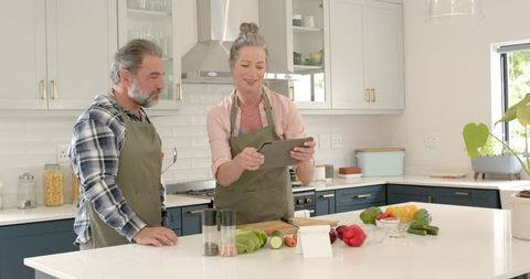 Senior Couple Cooking Meal Together in Modern Kitchen Using Tablet