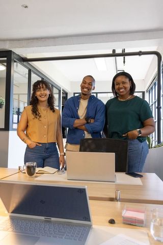 Diverse coworkers standing behind wood desk in modern office smiling and collaborating