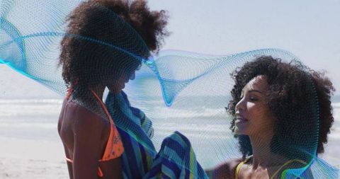 Mother helping daughter with towel on sunny beach shore, joyful summer family moment