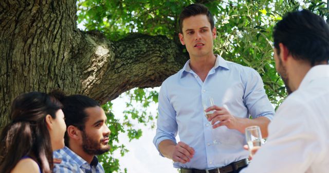 A group of friends is enjoying a relaxed conversation outdoors under a large tree. This image can be used for promoting social gatherings, casual meetups, outdoor events, and nature-themed activities. It would be great for content about friendship, leisure activities, and lifestyle blogs.