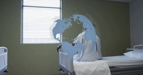 Senior woman sitting on hospital bed wearing gown facing window blinds in hospital room