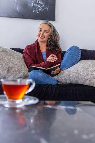 Cozy senior woman writing in journal on sofa with teacup lifestyle portrait