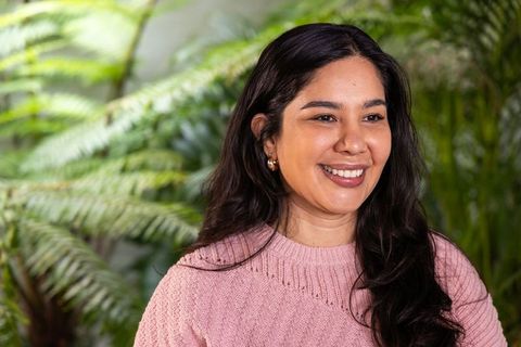 Smiling indian woman wearing pink knit sweater and gold hoop earrings looking off-camera in garden