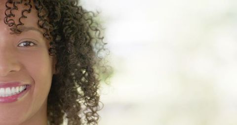 Smiling woman closeup with curly hair showing white teeth and lipstick, sunlit bokeh
