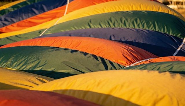 Vibrant hot air balloon envelopes unfolding at sunrise, stitched curves, colorful texture
