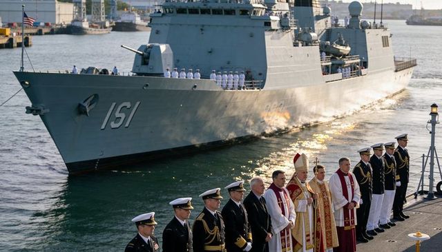 Naval officers and clergy standing on pier during sunlit warship commissioning ceremony by harbor 15