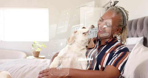 Senior woman cuddling small dog on bed with augmented reality pet care overlays, cozy bedroom bond