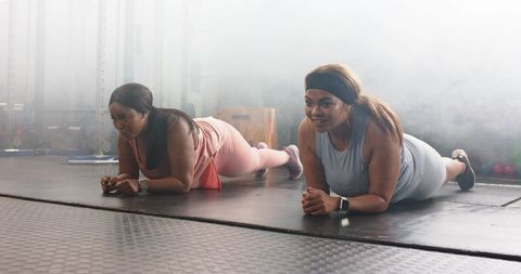 Midadult women performing forearm plank partner workout in gym building core strength