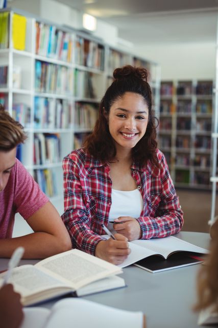 Schoolgirl smiling while studying with classmates in library. Ideal for educational content, school promotions, academic articles, and teamwork-related materials.