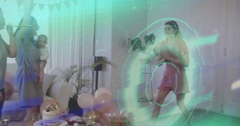 Woman in pink dress dancing under neon green projection at home birthday party with cake
