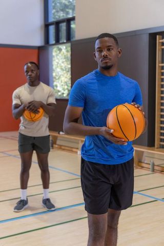 African american men practicing basketball on indoor court holding basketballs