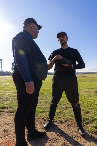 Senior coach mentoring middle-aged player during baseball practice on sunny field