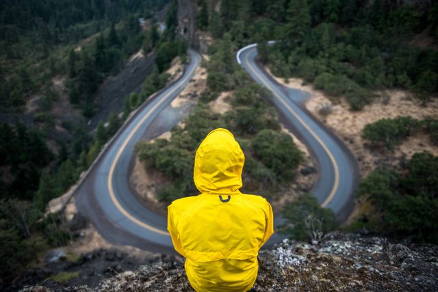 Adventurer in Yellow Raincoat Overlooking Mountain Curved Road - Download Free Stock Photos Pikwizard.com