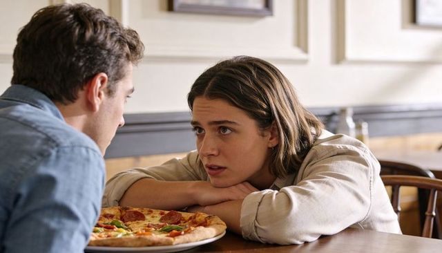 Young woman leaning on folded arms looking at partner over pepperoni pizza in pizzeria