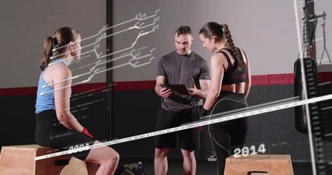 Coach reviewing tablet with two female athletes in gym during strength training session