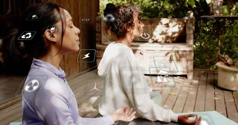 Two women meditating on wooden deck with augmented reality wellness icons, outdoor calm