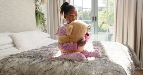 Young Girl Embracing Teddy Bear on Cozy Bed with Sunlit Background