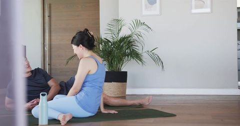 Couple practicing gentle home yoga sitting on mat chatting and relaxing with plant