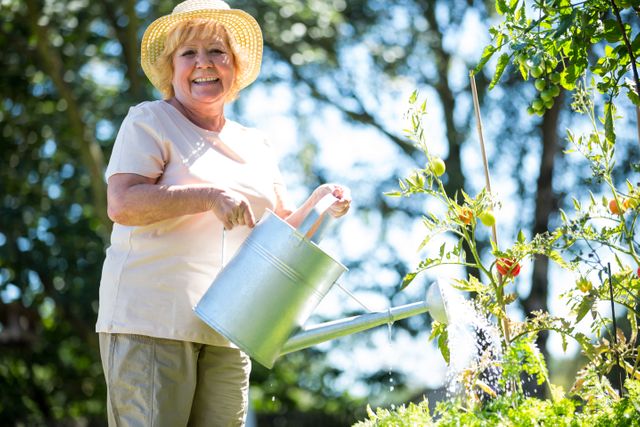 Senior woman enjoying gardening by watering plants with a watering can on a sunny day. Ideal for use in articles or advertisements about healthy lifestyles, retirement activities, outdoor hobbies, and gardening tips. Perfect for illustrating the joy of spending time in nature and promoting active living among seniors.
