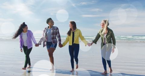 Diverse Female Friends Holding Hands Walking Along Sunny Beach