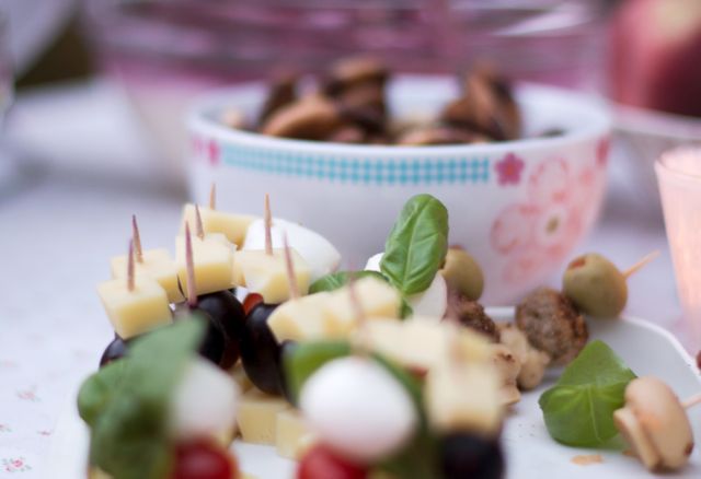 This image captures a beautifully presented assortment of finger foods, perfect for social gatherings and parties. Featuring cheese cubes, olives on skewers, grapes, and mozzarella balls, the arrangement offers an appetizing and visually appealing option for event planners, caterers, and food bloggers. The close-up shot highlights the textures and colors, making it ideal for use in promotional materials for catering services, party planning brochures, or food-related blogs and websites.