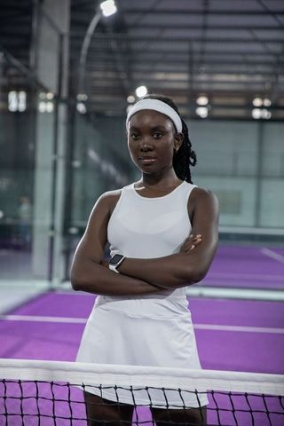 Confident african american female tennis player standing at net on purple indoor court