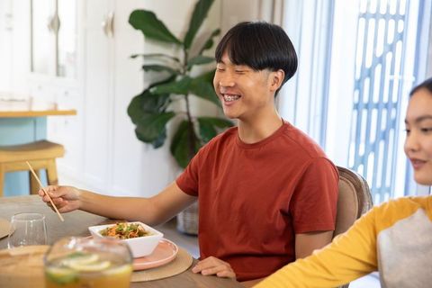 Asian friends enjoying meal together using chopsticks at home