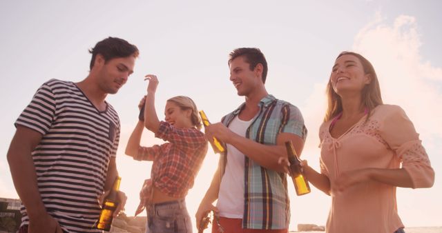 Group of young friends having fun at a summer outdoor party, holding beer bottles and laughing. Perfect for promoting lifestyle, friendship, summer events, social gatherings, and leisure time activities.