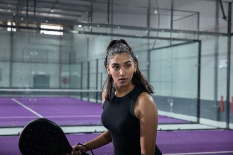 Focused indian female padel player holding racket on indoor purple court