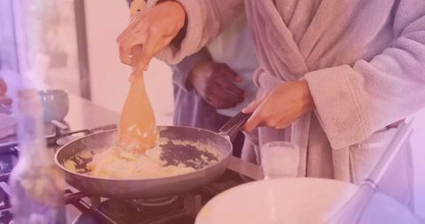 Woman cooking scrambled eggs in bathrobe as partner observes