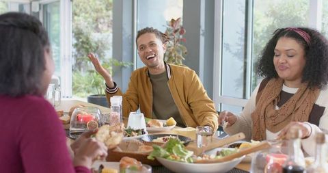 Multiethnic friends enjoying sunny casual lunch sharing salad and laughter at dining table