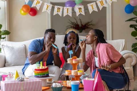 African american family celebrating birthday at home blowing party blowers around cake