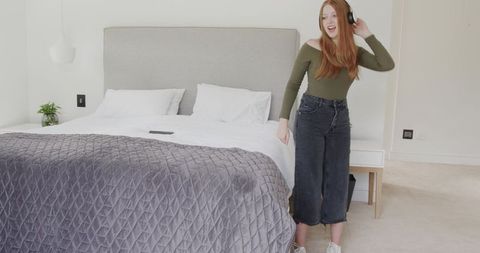 Redhead Woman Dancing with Headphones in Minimalist Modern Bedroom with Smartphone