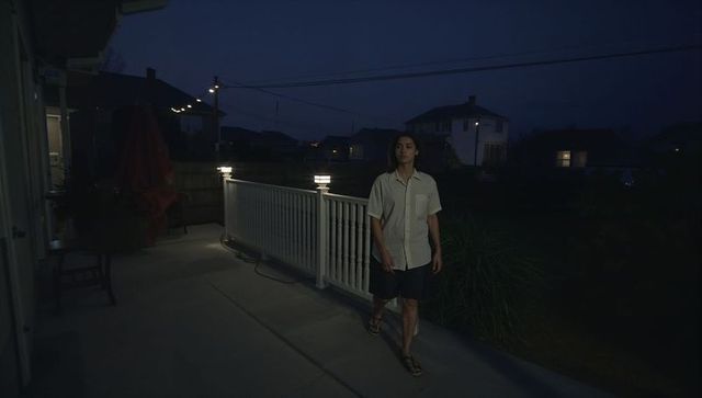 Walking man along illuminated porch railing at night in suburban neighborhood