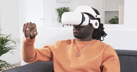 African American man wearing white VR headset pointing while sitting on modern sofa