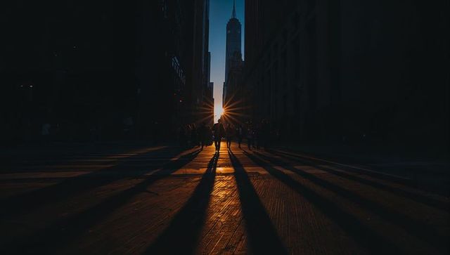 Sunburst between skyscrapers casting long shadows across urban crosswalk at dusk