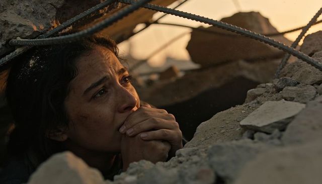Woman trapped under rubble at sunset holding hands to mouth conveying fear and resilience