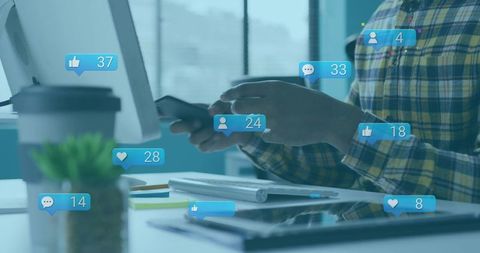 Young professional in plaid shirt scrolling smartphone at desk with social notifications